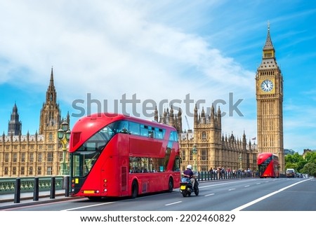 Red double-decker buses pass by Big Ben and the Houses of Parliament on Westminster Bridge. London, England
