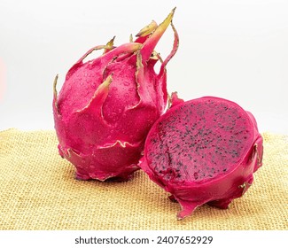 Red dragon fruit, aka Pitaia or Pitaya. Red pitayas on a jute fabric, one of the fruits being cut in half showing the fruit pulp.