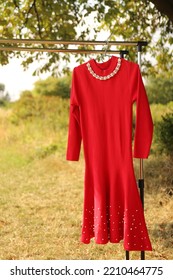 A Red Dress With Decor Hangs On A Hanger.