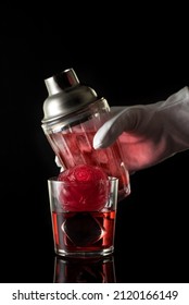 Red Drink With Ice, Bar Shaker And Bartender's Hand, Black Background. Summer Cold Alcoholic Soft Drinks, Drinks And Cocktails.