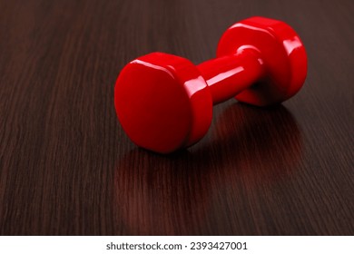 A red dumbbell lies on a wooden surface. Angle view. Selective focus. - Shutterstock ID 2393427001