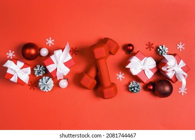 Red Dumbbells With Winter Decorations And Gifts On Red Background. Top View Christmas Fitness Composition With Copy Space.  