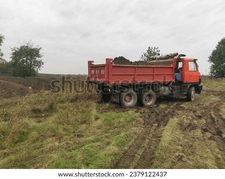 A red dump truck carrying soil across a meadow