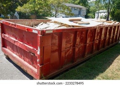 Red dumpster full of building debris on a street in front of a house