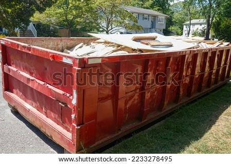 Red dumpster full of building debris on a street in front of a house