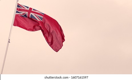 The Red duster Flag otherwise know as Red Ensign, flying in the sea breeze. The union Jack is in the top left corner. The flag is on the left hand side with negative space to the right in light red.