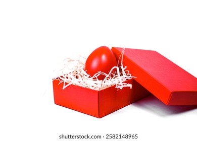Red Easter egg in a gift box with decorative straw on a white background.