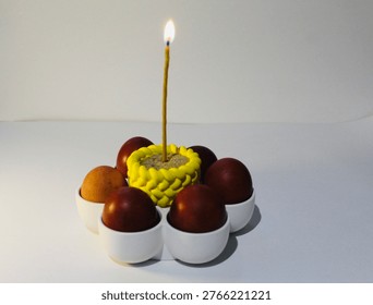 Red Easter eggs arranged in circular flower composition with a central candle on clean white background.