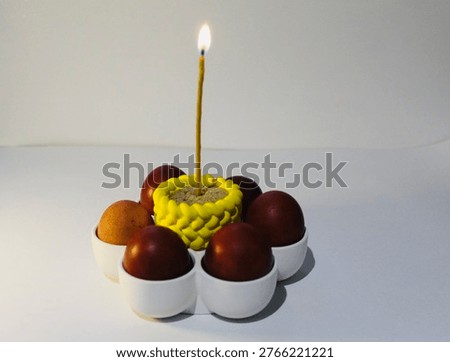 Red Easter eggs arranged in circular flower composition with a central candle on clean white background.