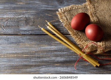 Red easter eggs and beeswax candles on burlap over rustic wooden table for holiday tradition