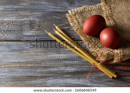Red easter eggs and beeswax candles on burlap over rustic wooden table for holiday tradition