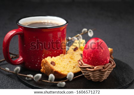 Red Egg in a wicker stand, Easter cake and cup of coffee on black slate dish and painted eggs on the table - traditional Easter breakfast