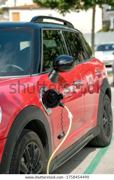 Red electric\
car at charging station with the power cable supply plugged on\
blurred background. Power supply connect to electric vehicle.\
Eco-friendly alternative\
energy.
