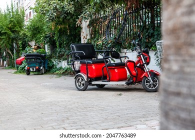 Red Electric Rickshaw Or E-rickshaw Commercial Vehicle Display With Selective Focus Under Daylight At Kemer, Turkey. Rent Transport For Tourists.