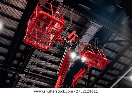 Red elevated work baskets displayed indoors beneath a steel roof structure, ideal for contractor access, safety training, and fleet marketing