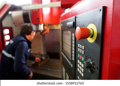 red emergency button focused on the keypad of a CNC milling machine, while the operator is clamping a vise - Powered by Shutterstock