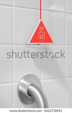 Red emergency button with handrail on wall in the disabled toilet. Security and assistance for disabled, senior concept. Emergency button in a special toilet for pregnant woman, elder and disabled.	