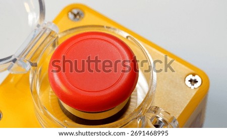 Red emergency stop push button with clear protective cover open enclosure, industrial mushroom switch on machinery control panel, safety shutdown device close up detail, emergency abstract concept