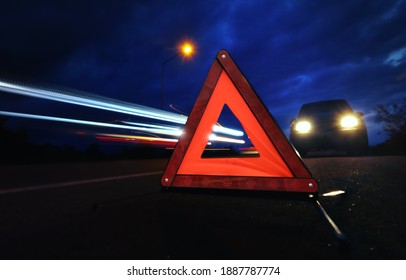 Red emergency stop sign (red triangle warning sign) with long-exposure of traffic light trails at nigh. - Shutterstock ID 1887787774