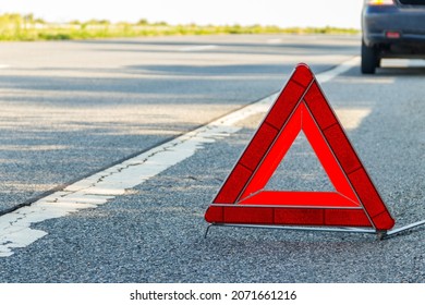 Red emergency stop sign (red triangle warning sign) and broken car on a road