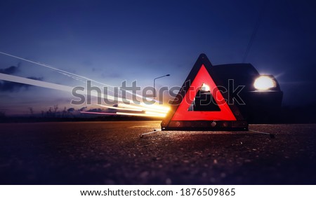 Red emergency stop sign (red triangle warning sign) with long-exposure of traffic light trails at nigh.