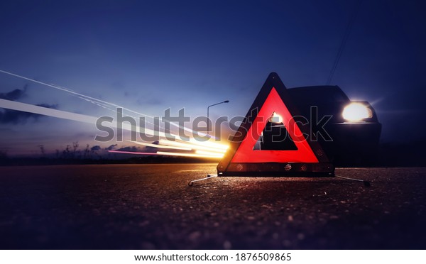 Red emergency stop sign\
(red triangle warning sign) with long-exposure of traffic light\
trails at nigh.