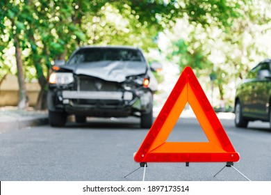 Red emergency stop triangle sign on road during a car accident. Broken gray car in road traffic accident. Car crash traffic accident on city road after collision