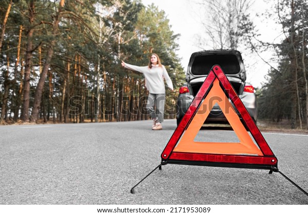 Red emergency triangle with blurred car and woman\
calling car mechanic in the background. Accident and broken car on\
the road