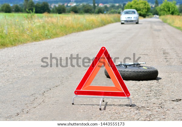 Red emergency\
triangle stop sign on the road. Spare wheel and wheel wrench on a\
backdrop. Oncoming traffic.\
