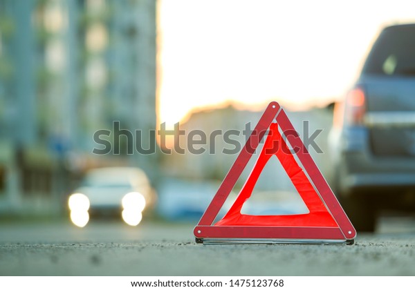 Red emergency triangle stop sign and broken car
on a city street.