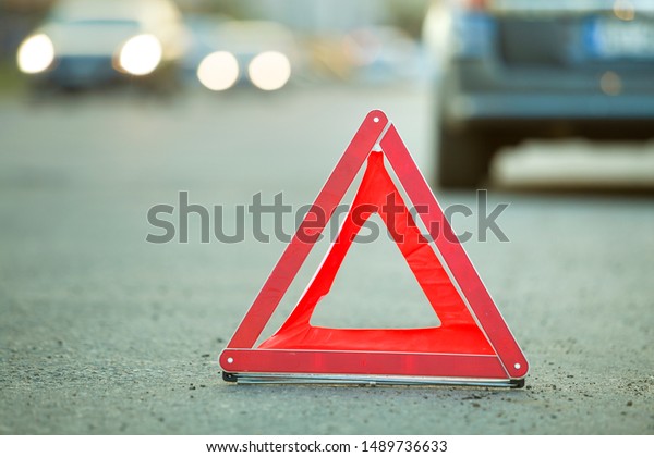 Red emergency triangle stop sign and broken car\
on a city street.