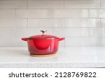 Red enameled cast iron covered round dutch oven on a granite counter top against a ceramic background