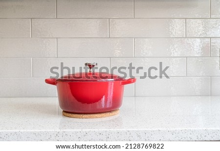 Red enameled cast iron covered round dutch oven on a granite counter top against a ceramic background