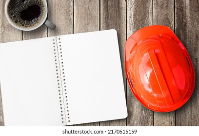 Red engineer safety helmet and blank notebook with coffee overhead view. Construction of brown wooden texture background space for design