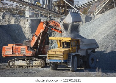 Red excavator pouring crushed stone out of a bucket into a dump truck body, closeup. Heavy mining equipment.