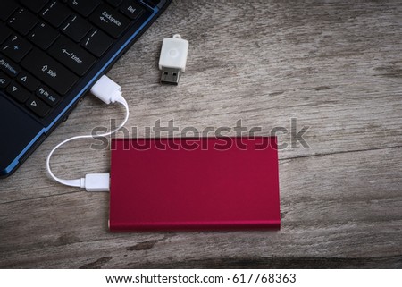 Red external hard drive (HDD) connected to laptop for transfer or backup data on wooden desktop with copy space