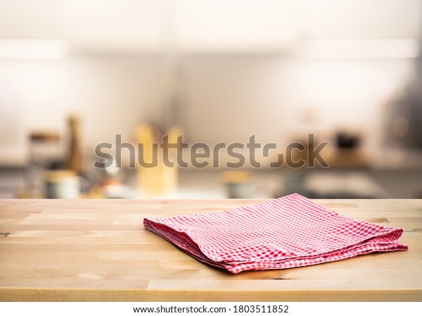 Red fabric,cloth on wood table top on blur
kitchen counter (room)background.For montage product display or
design key visual layout.
