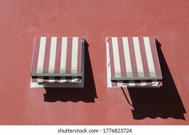 red facade with two windows with red and white striped awnings and shade