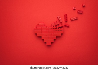 Red falling apart heart symbol made of plastic building blocks. Flat lay image of breaking down like button on red background. Minimalist photo of stylized dissolving love symbol.