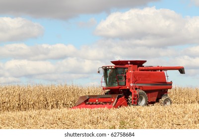 Red Farm Combine Harvesting Corn Against A Blue Sky With Clouds