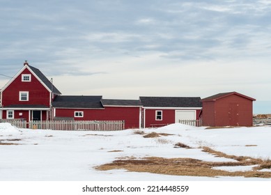 A red farm house with multiple additions and outcrop buildings with a grassy meadow in the foreground. It's winter with white snow on the ground. The buildings have black roofs, and white windows. - Shutterstock ID 2214448559