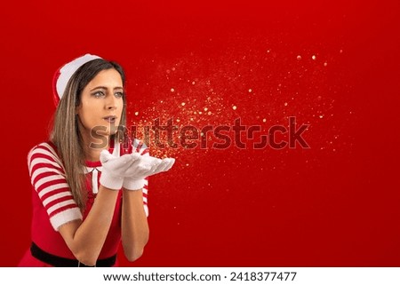 Red female santa blowing golden dust particles with white gloves and red background.