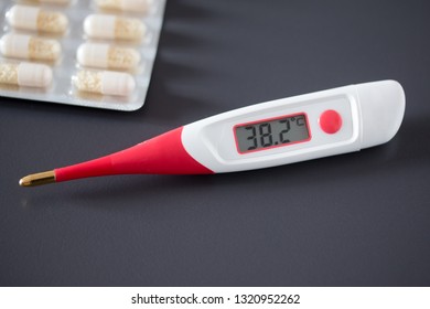 Red fever thermometer with digital display and pills lying on the desk - Shutterstock ID 1320952262
