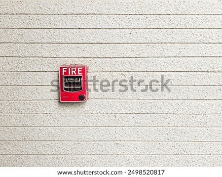 a red fire alarm pull station mounted on a beige textured wall.