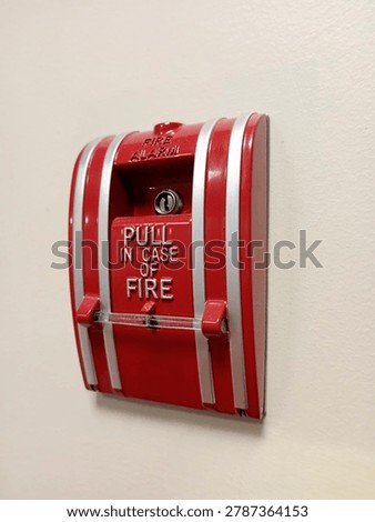 A red fire alarm pull station is mounted on a wall. It is used to alert for a fire in case of an emergency. This device is important for safety.