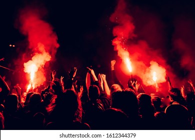 Red fire in the crowd. People raising hands and partying at concert. Red flame in the dark.