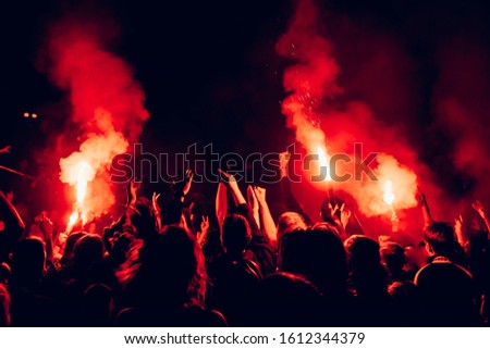 Red fire in the crowd. People raising hands and partying at concert. Red flame in the dark.