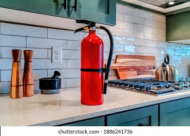 Red Fire Extinguisher Beside Cooktop On The Countertop Inside Kitchen Of Home