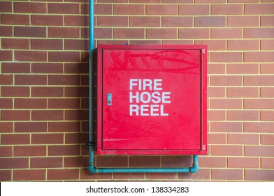 Red fire hose reel, mounted on a brick wall background.