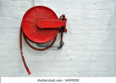 Red fire hose reel, mounted on a white wall background.